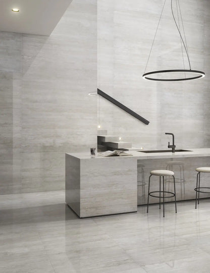 Cocina de diseño minimalista con una elegante lámpara circular sobre la barra. Dos sillas altas complementan el espacio. Toda la cocina está revestida con un elegante acabado de piedra pulida, creando un ambiente moderno y sofisticado.
