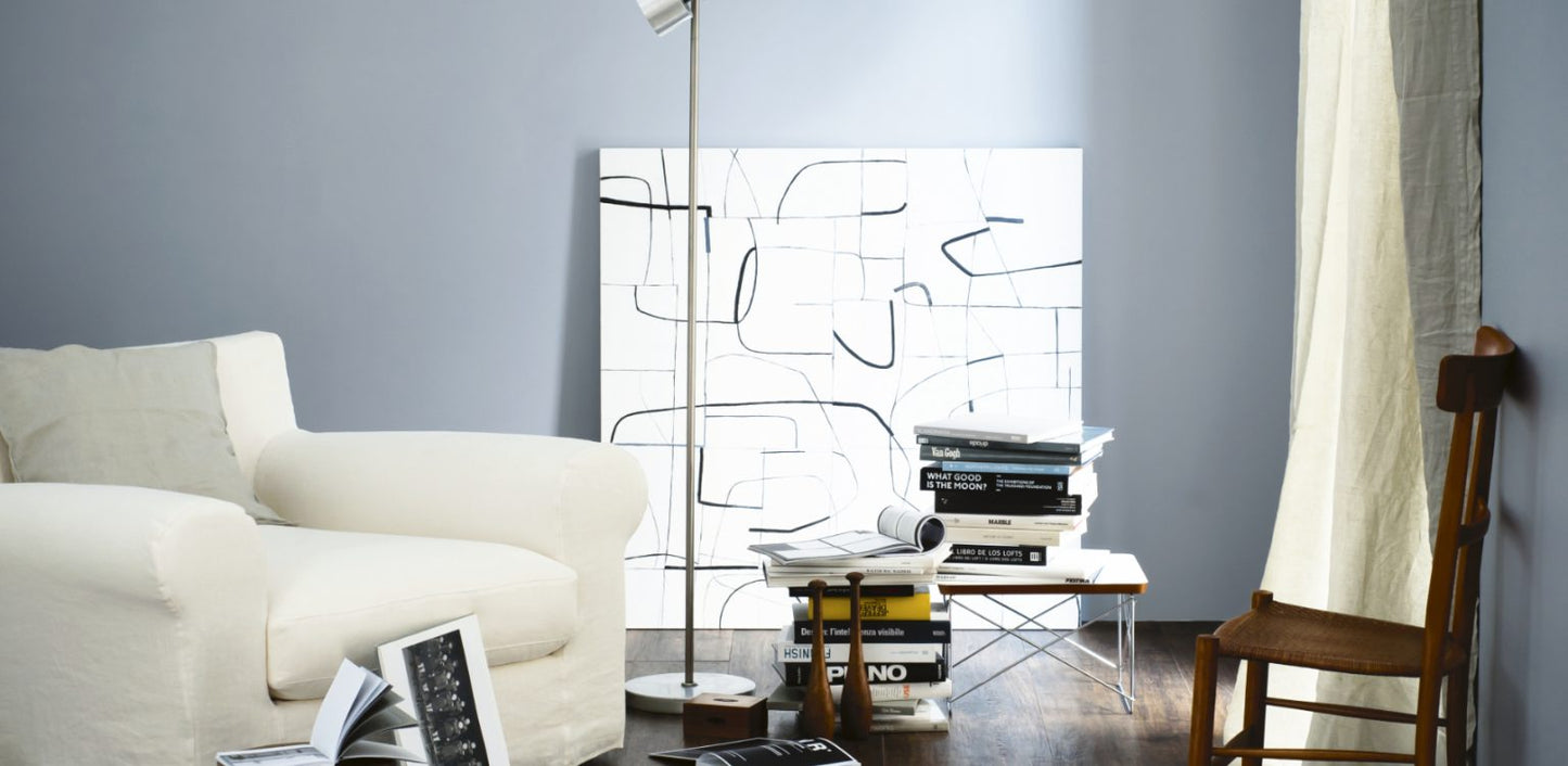 Sala con un sillón blanco, una gran colección de libros y una lámpara de pie. Un cuadro abstracto se destaca en una pared de color gris.