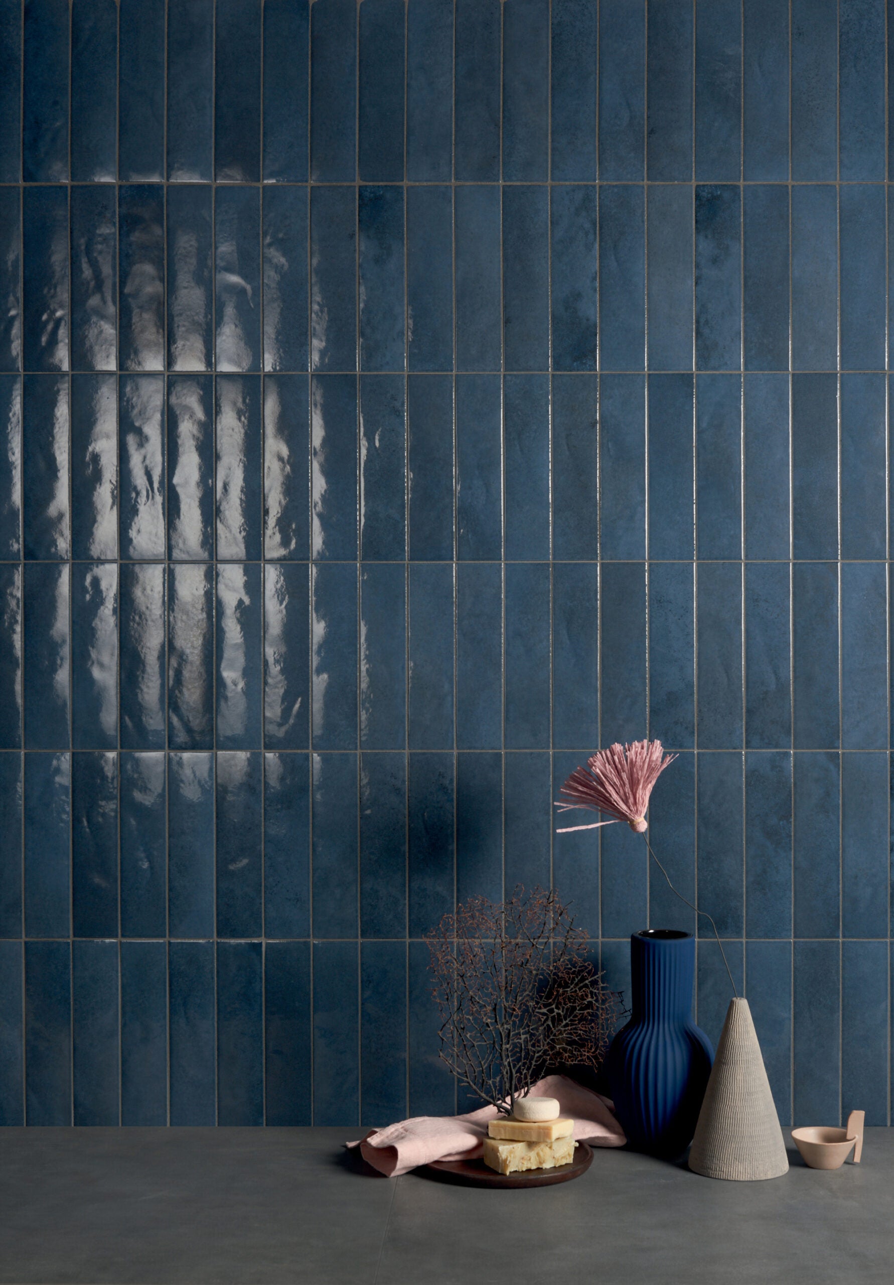 Muro con azulejo azul oscuro con acabado brillo, accesorios en tonos azules, rosas y grises que resaltan entre si. 