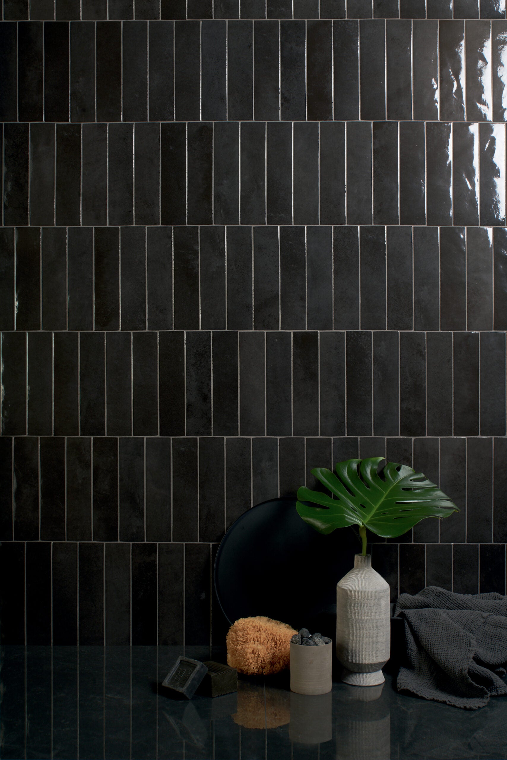 Muro revestido con azulejos de color negro de alto brillo, acentuado con accesorios decorativos en tonos gris, verde y negro que destacan y se complementan entre sí.