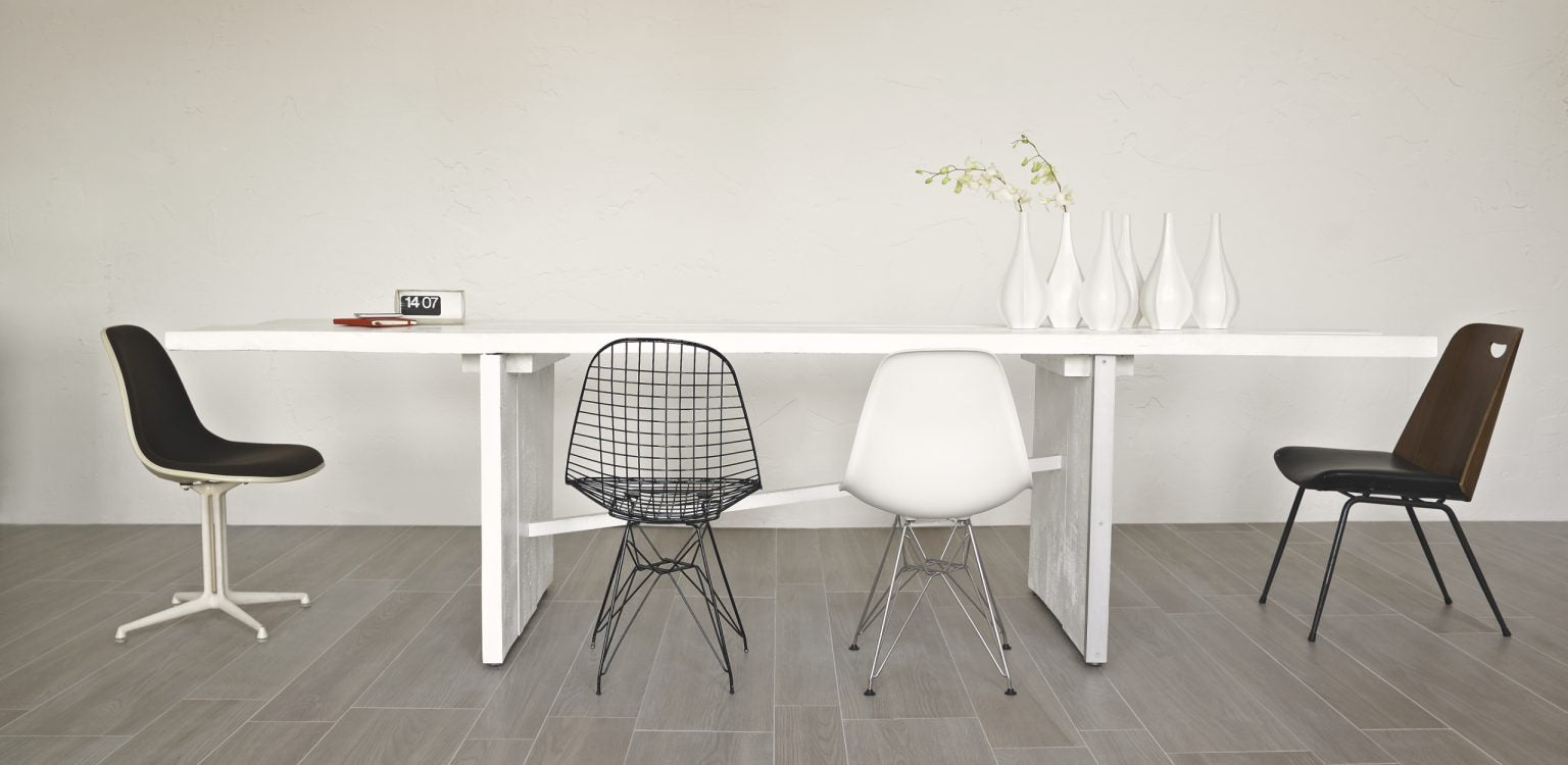 Comedor de estilo minimalista con sillas en blanco y negro, accesorios blancos en la mesa y suelo de madera en tono gris, creando un ambiente sencillo y elegante en el hogar