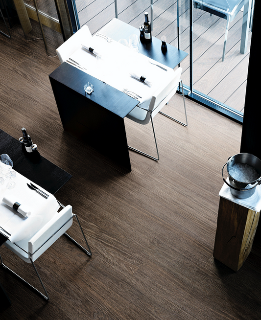 Restaurante con vista a la terraza, mobiliario en elegante negro y sillas blancas que resaltan sobre el suelo de madera, creando un ambiente acogedor y moderno